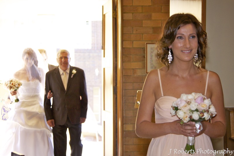 Bridesmaid walking down the aisle with bride and her father in the background - wedding photography sydney